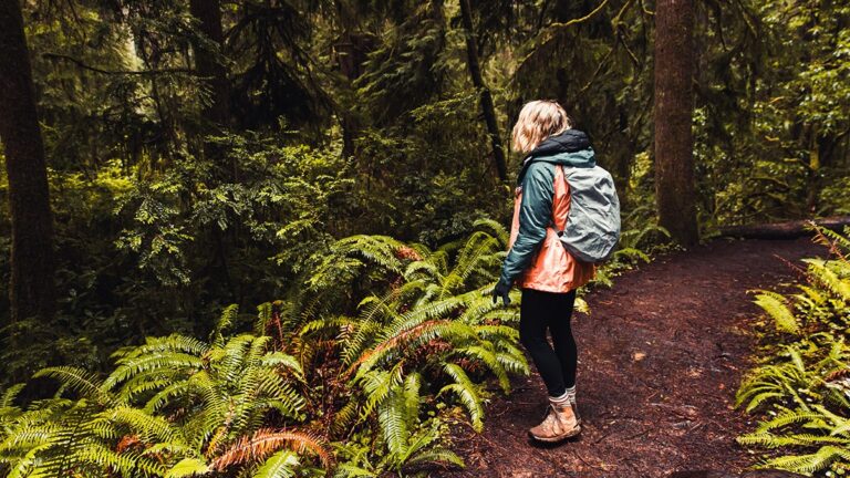 What to wear to the Oregon Coast by season - Woman on a hiking trail wearing raincoat with a backpack