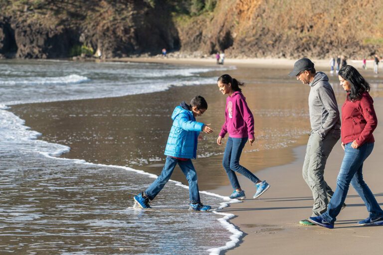 A family walking on the beach wearing jackets and long pants as an example of what to wear in March, April and May on the Oregon Coast