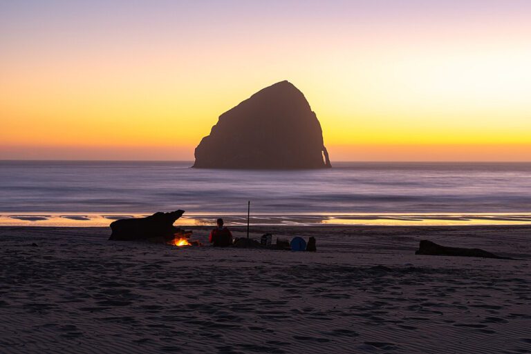A beach campfire with Haystack Rock in the background at sunset on Cape Kiwanda in Pacific City, Oregon