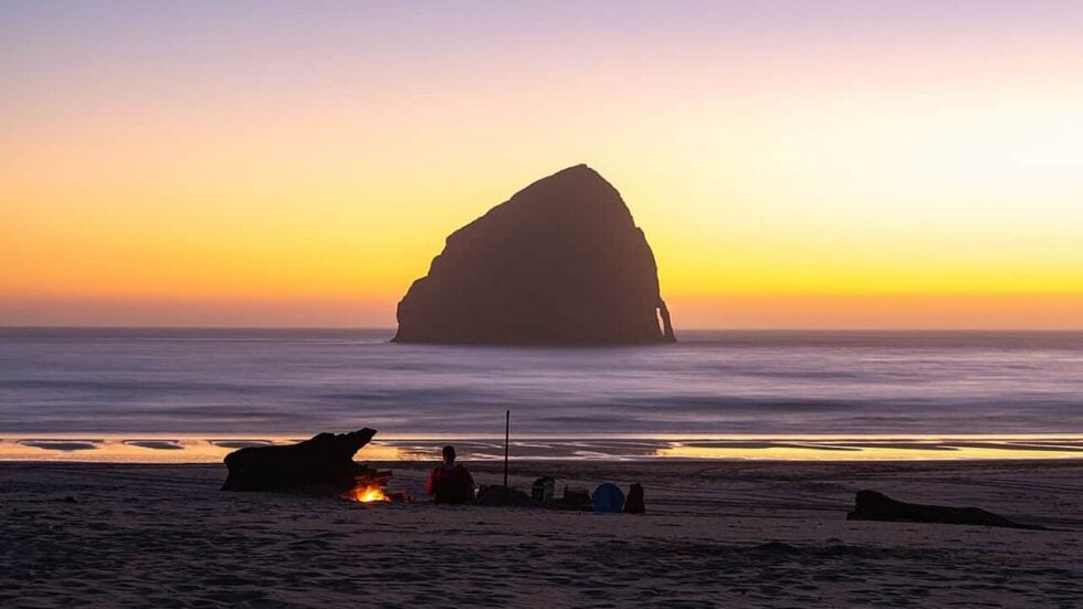 A beach campfire with Haystack Rock in the background at sunset in Pacific City, Oregon near Cape Kiwanda